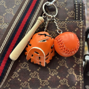 Detailed view of mini orange baseball glove and wooden bat keychain on a branded bag
