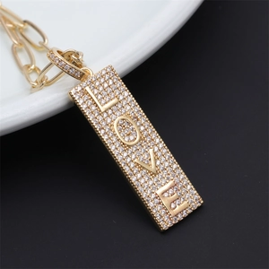 Macro shot of gold rectangle LOVE pendant with pavé crystals on a white ceramic plate
