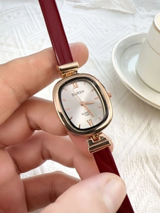 Close-up of vintage oval quartz watch with burgundy leather strap and golden case