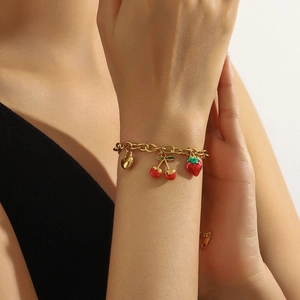 Gold chain bracelet with red enamel strawberry and cherry charms worn on a wrist