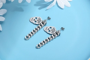 Silver skull drop earrings with chunky Cuban link chains on a light blue background