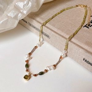 Macro detail of a 18k gold plated necklace with green gemstones and baroque pearls