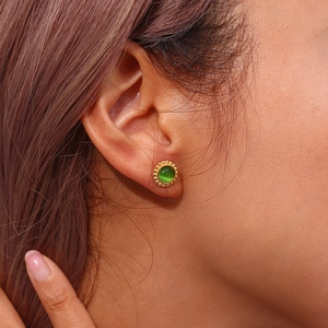 Detail of a gold sunburst earring with a green cat-eye stone worn on a model's ear