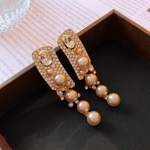 Dettaglio di orecchini pendenti con perle champagne e strass su legno scuro