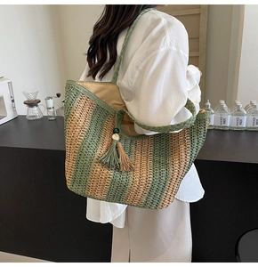 Detailed side view of green striped straw tote bag with tassels in a minimalist setting
