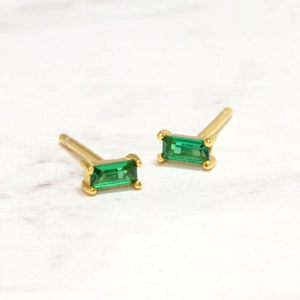 Macro shot of gold rectangle earrings with green emerald-cut gemstones on marble background