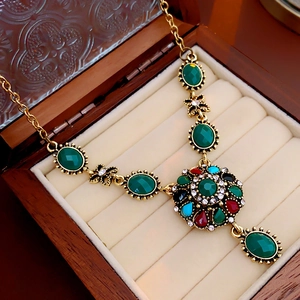 Macro shot of a vintage gold necklace with colorful floral pendant and green gemstones