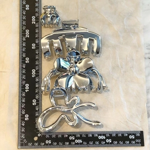 Detailed size comparison of metallic silver flower and bow hair claws against a ruler