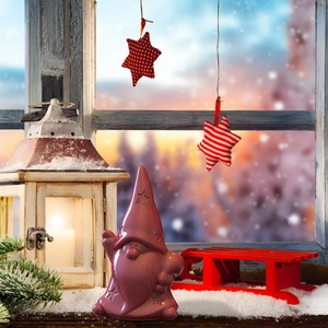 Ceramic pink gnome ornament on snowy windowsill with warm holiday lights