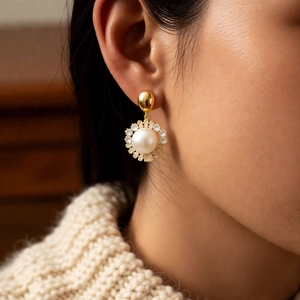 Close-up of elegant gold-plated pearl pendant earrings worn with a knit sweater