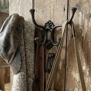 Vintage cast iron wall hook with four movable hooks and decorative scrollwork on wood