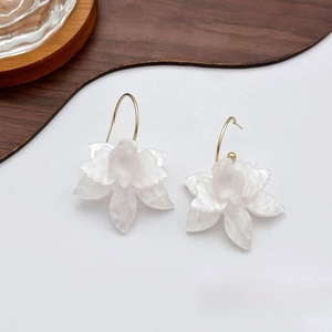 Detail of white flower earrings with pearlescent petals and gold hooks on wood tray