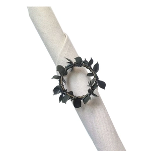 Rustic green leaf wreath napkin ring on beige linen cloth with dark vine metal design