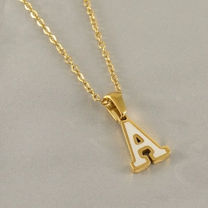 Detail of a golden letter A pendant with white enamel inlay on a delicate O-chain necklace