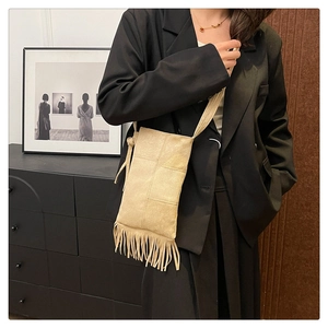 Detail shot of beige faux suede tote bag featuring long tassel fringe and a slim shoulder strap
