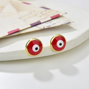 Golden round evil eye stud earrings with vibrant red enamel on white ceramic display