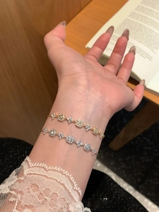 Detail of 18K gold and silver plated floral zircon bracelets on wrist over a wooden desk