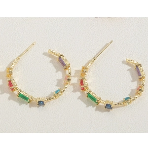 Golden C-shaped heart hoop earrings with colorful zircon stones on textured metal surface