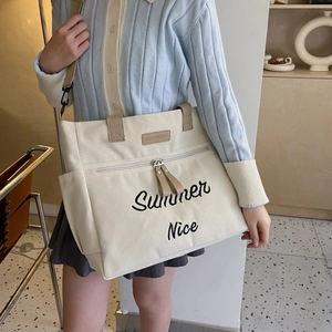 Detail of beige canvas tote bag with adjustable shoulder strap and embroidery on model