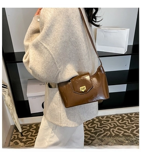 Deep brown glossy leather baguette bag with golden buckle shown on a model