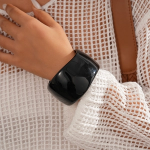 Close-up of a wide glossy black resin bangle on a wrist with minimalist geometric design