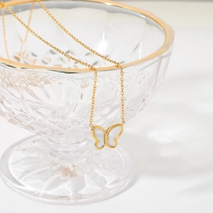 Detailed shot of a 14K gold butterfly pendant necklace draped on a glass bowl rim