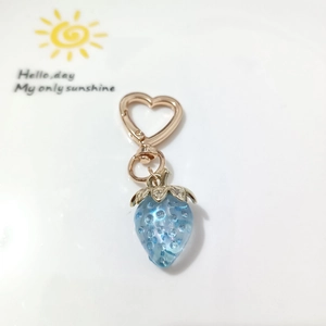 Close-up of a blue strawberry keychain with heart-shaped hook and golden metal finish