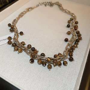 Detailed close-up of tiger eye bead clusters on a silver chain necklace with a paper tag