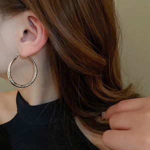 Close-up of textured silver hoop earrings with wave patterns on a female model