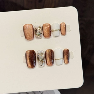 Detail of handmade bronze cat-eye and white press-on nails with gold star glitters