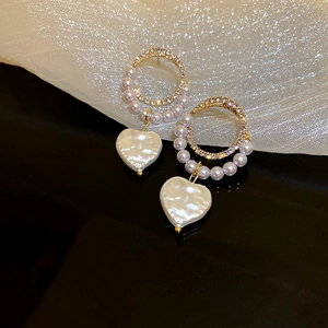 Macro shot of gold hoop earrings with white pearls and sparkling heart pendants