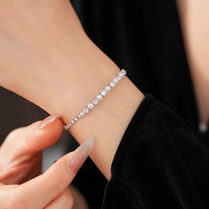 Macro shot of a zirconia and pearl chain bracelet worn on a wrist against dark fabric