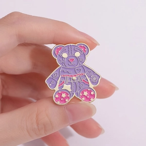 Close-up of a purple cartoon bear enamel pin with heart and flower details