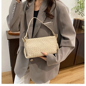 Dettaglio della trama intrecciata sulla borsa beige indossata con blazer grigio