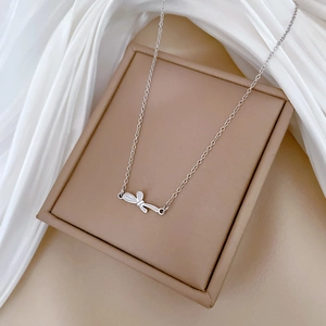 Macro detail of silver bow pendant necklace resting on a beige jewelry box with silk