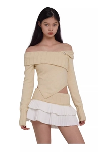 Detail view of beige off-shoulder knit top with metal buckle and white pleated skirt