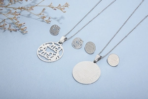 Detail of silver titanium steel MAMA pendant necklace set with stud earrings on blue background