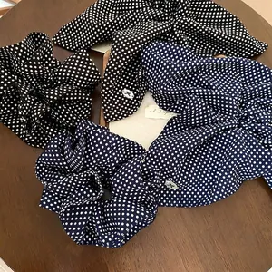Polka dot fabric scrunchie and bow headband set in black and navy on a wooden table