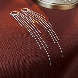 Détail macro de boucles d'oreilles à franges argentées avec chaînes serpent sur tissu