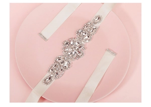 Close-up of bridal belt with crystal floral patterns and ivory satin ribbons on pink tray