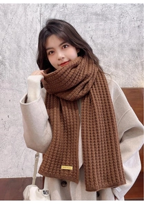 Macro view of brown knitted winter scarf showing detailed stitch texture and handmade label