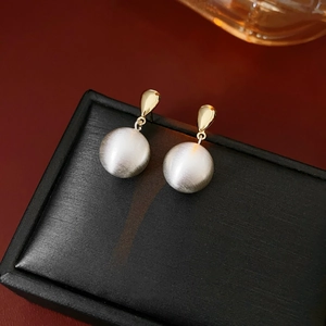 Détail de boucles d'oreilles pendantes plaquées or avec une sphère blanche brossée