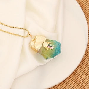 Macro detail of Hamsa hand pendant with natural green crystal on a gold twisted chain
