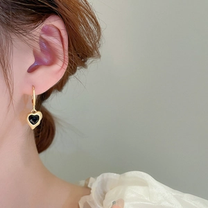 Detail shot of vintage gold heart earrings with black stone on model's ear