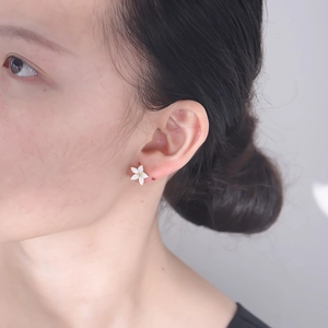 Close-up of elegant small white enamel flower earring worn on a female ear
