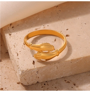 Detailed view of a gold hugging hands open ring on a natural travertine stone surface