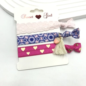 Three-piece hair tie set with pink lace, floral patterns, and tassel charms on white card