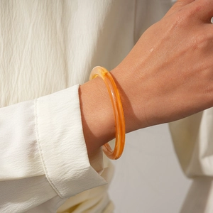 Minimalist amber-toned acrylic geometric bangle shown on model wrist with white shirt