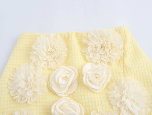 Dettaglio macro di gonna in tweed gialla con applicazioni floreali 3D bianche e texture