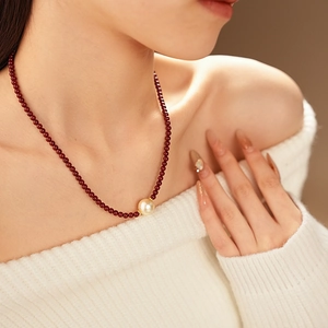 Détail d'un collier de perles rouges avec un pendentif perle dorée porté par un mannequin